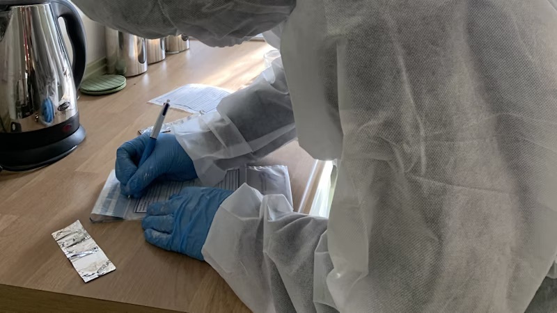 A student wearing protective clothing documenting evidence at the crime scene house