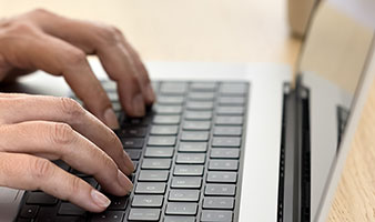 An older person typing on a laptop computer