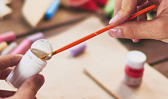 A person dipping a paintbrush into a small paint pot.