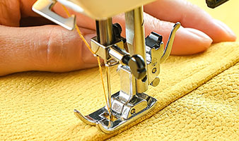 A person using a sewing machine to sew yellow fabric.