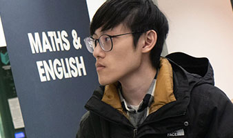 A student wearing glasses in front of a Maths and English pull up banner.