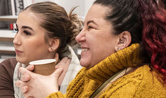 Two students chatting with other students laughing and holding a coffee