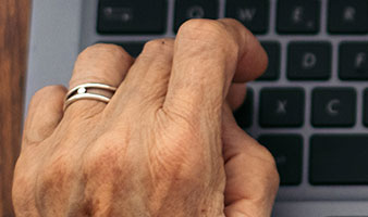 An older persons hand typing on a laptop