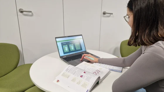 A young student studying A Level biology with a textbook open and laptop