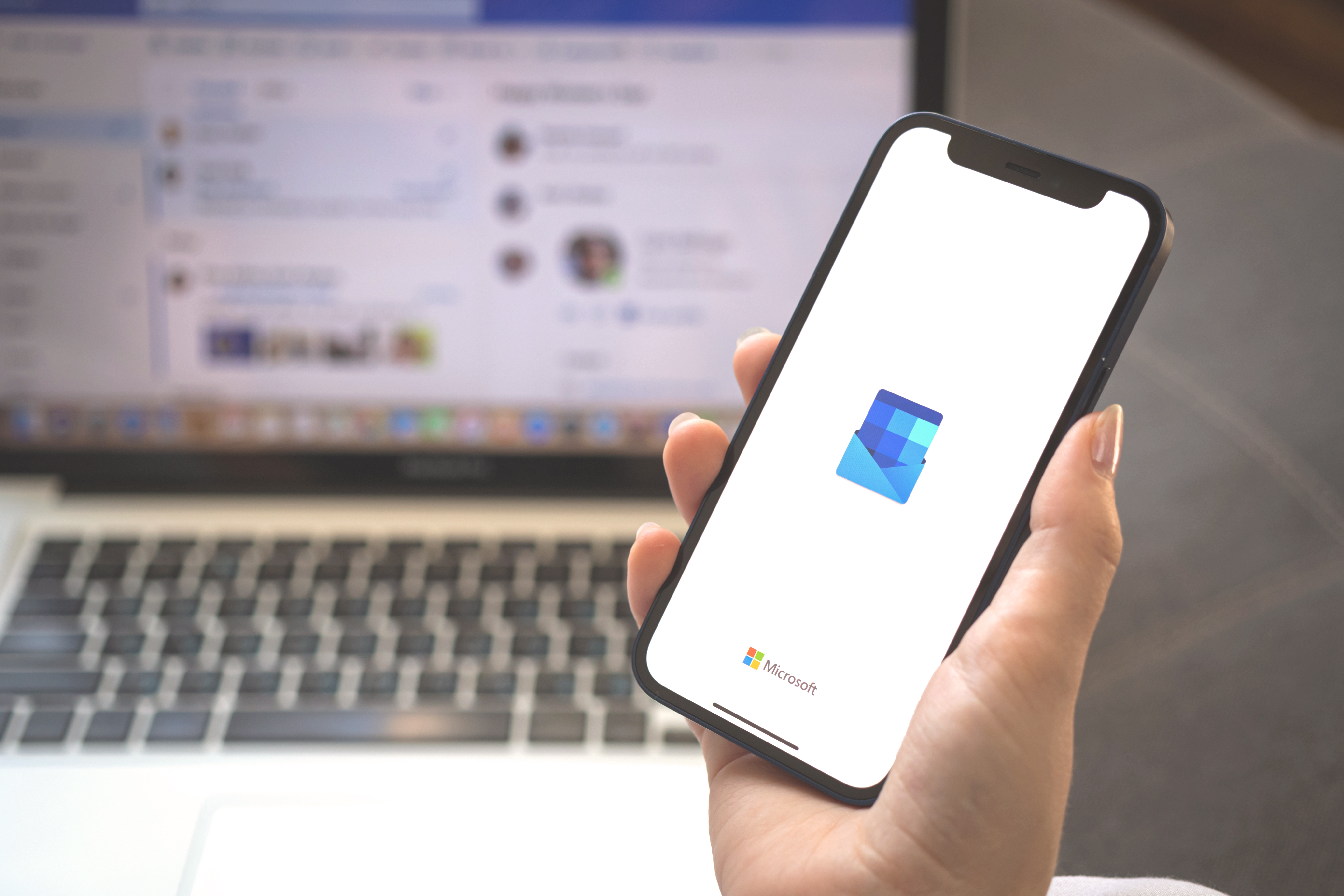 Person's hand holding a mobile phone showing the Microsoft Outlook app splash screen