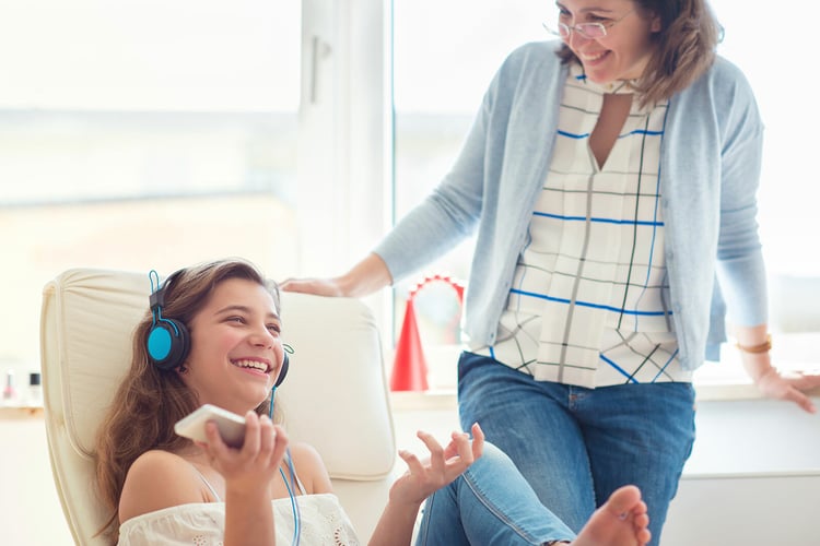 Teenage girl in headphones in lounge chair with smiling mom