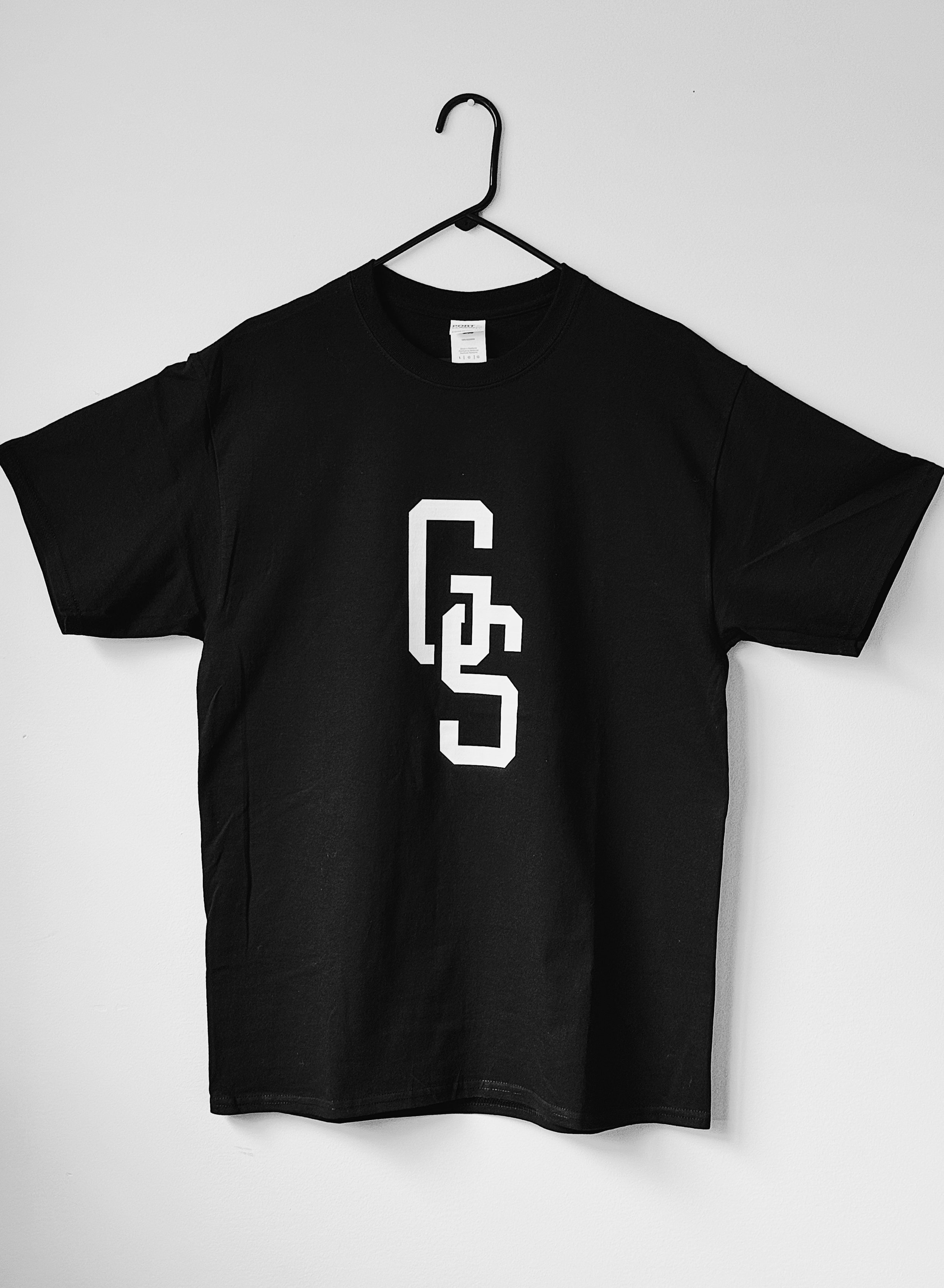 Black T-shirt with a white GS monogram design displayed hanging on a wall.