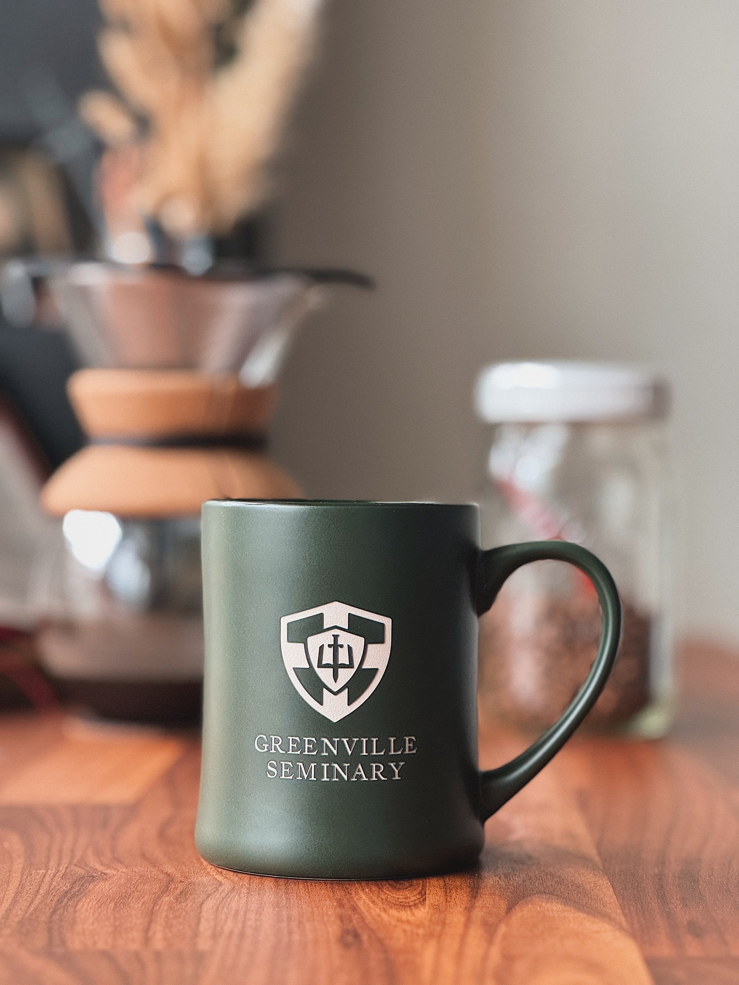 Dark green ceramic mug with the Greenville Seminary crest on a wooden table.
