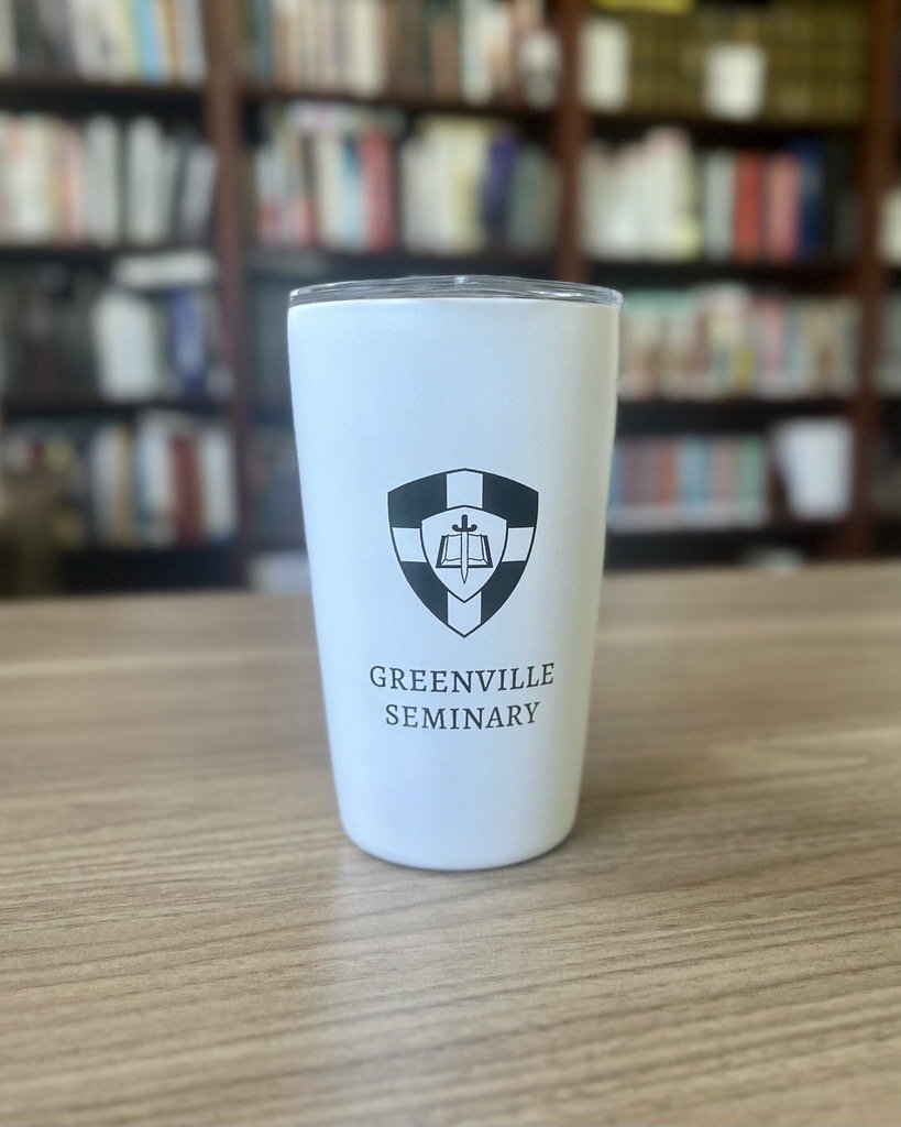White insulated Greenville Seminary tumbler photographed in a library setting.