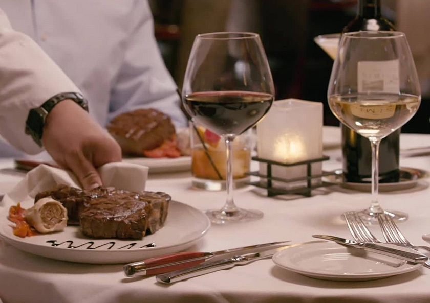 Steak dinners on table with glasses of wine.