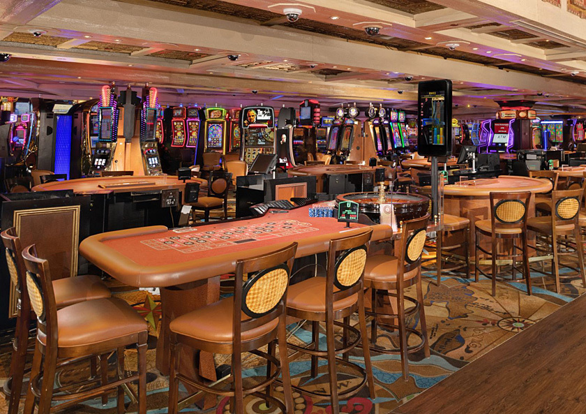 Wide image of casino floor with roulette table in forground