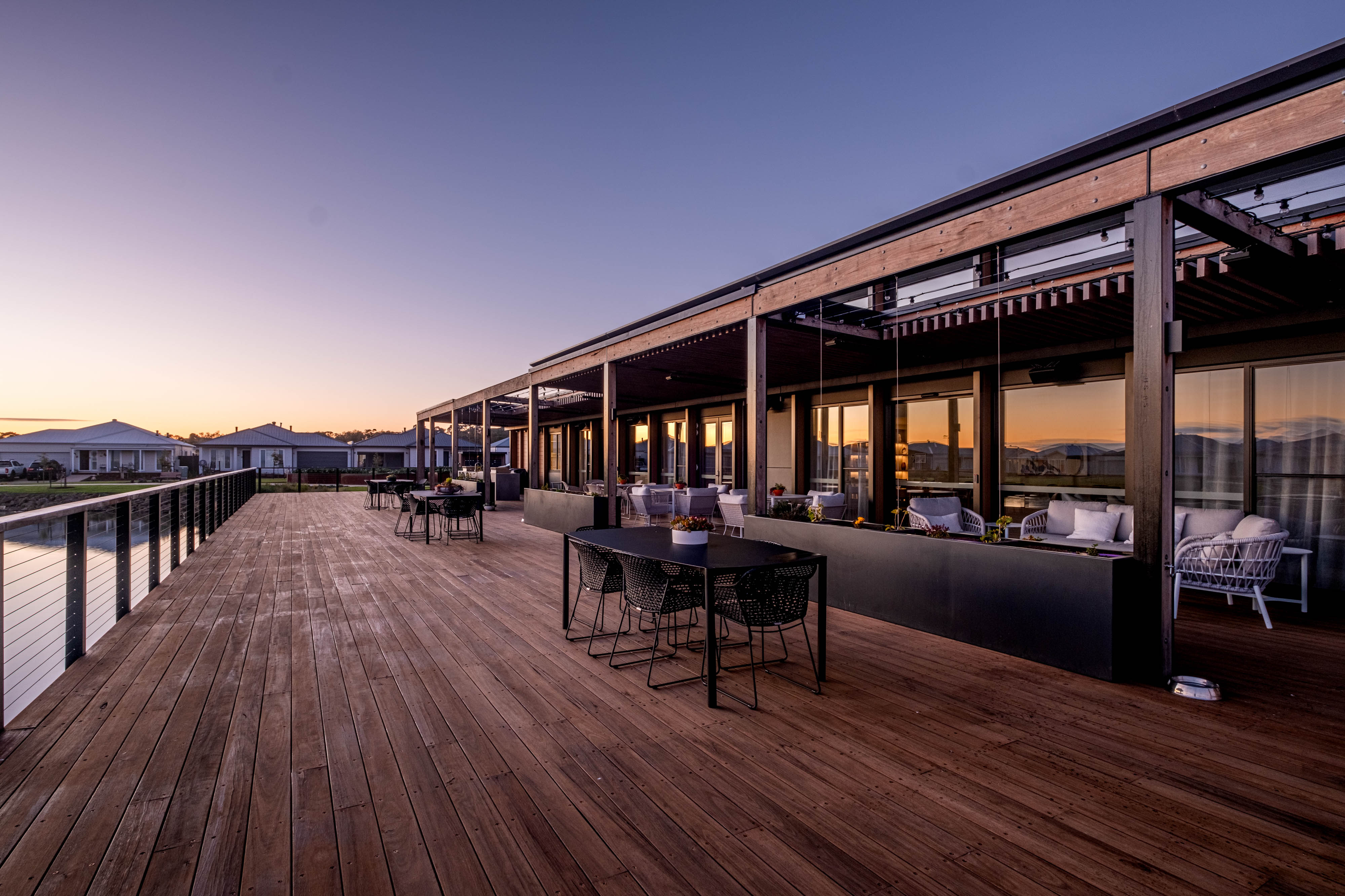 Modern waterfront deck with dining tables at sunset.