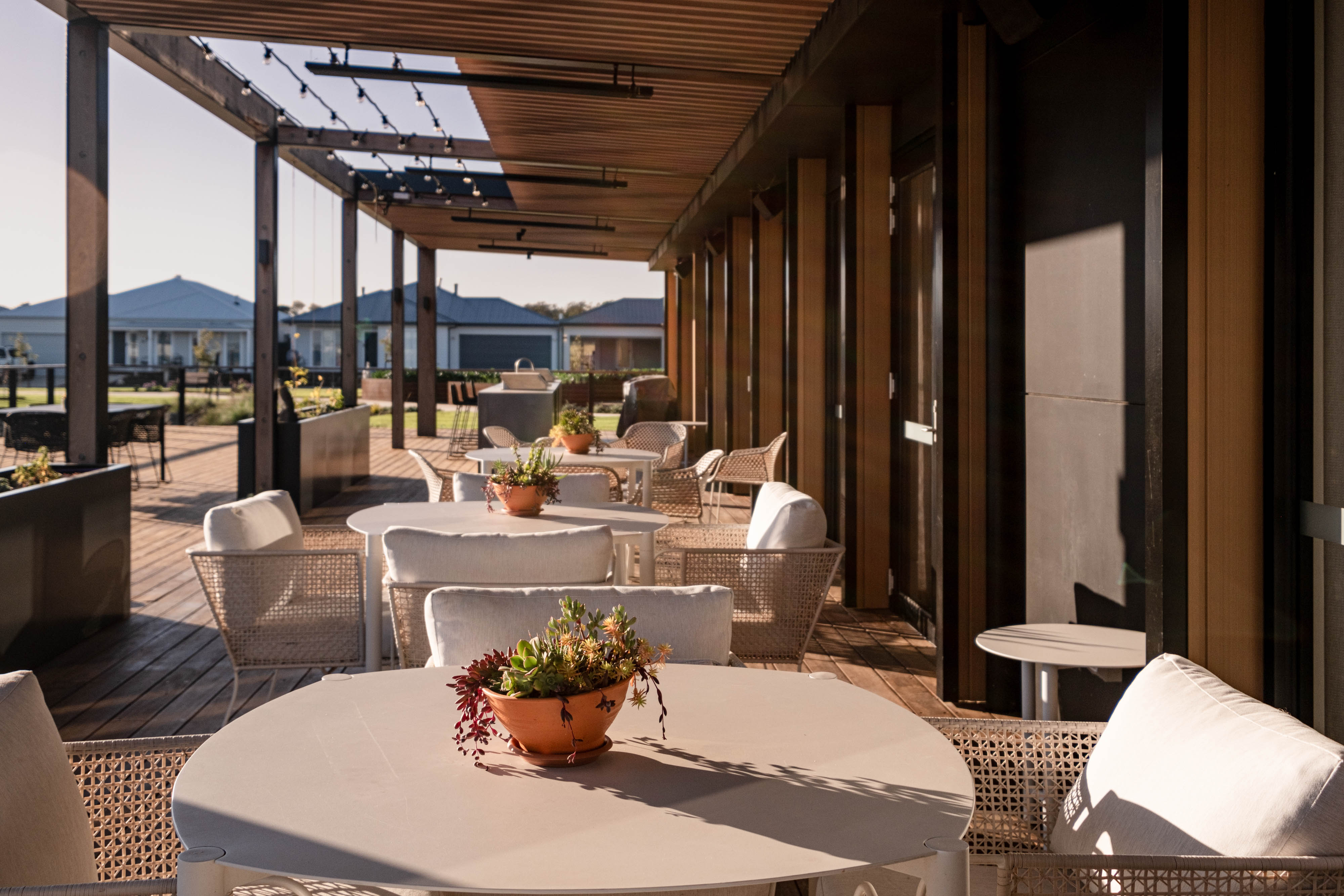 Outdoor alfresco with tables, chairs, pergola, and potted plants in a residential setting.