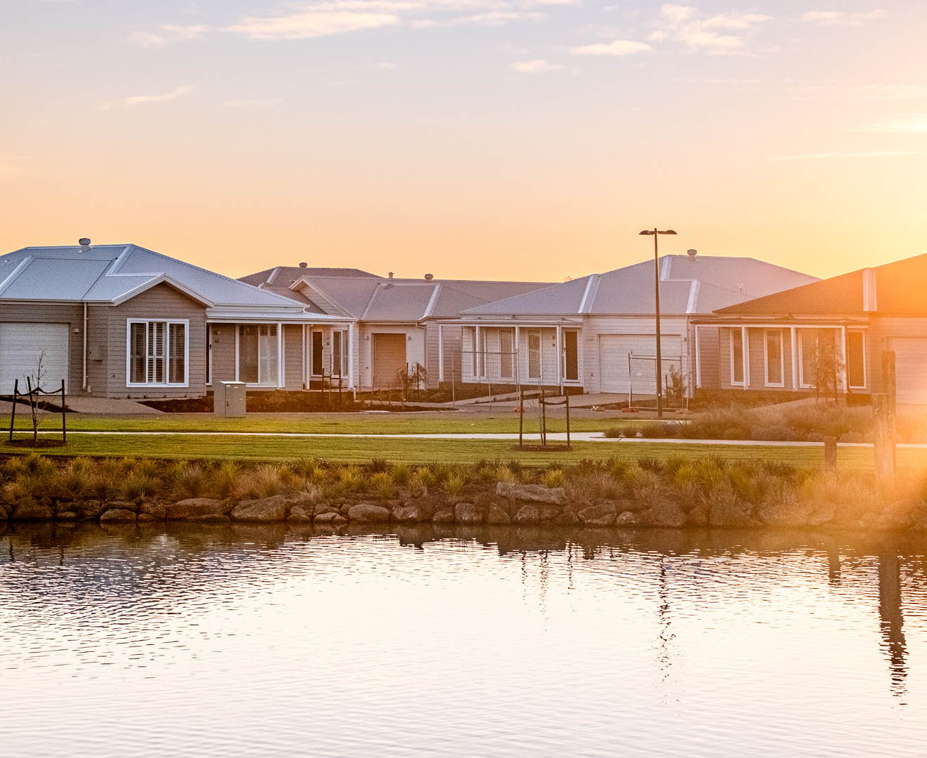 Modern homes at Lifestyle Communities Bellarine beside a calm lake at sunset