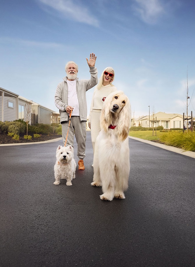 Couple walking their dogs and waving while enjoying a stroll through a Lifestyle Communities neighbourhood.