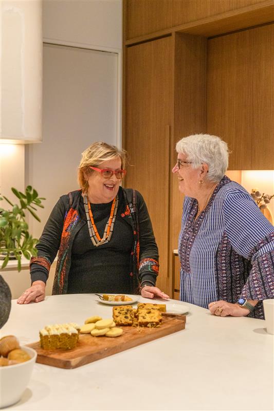 Two women chatting and enjoying homemade treats together in a modern kitchen at Lifestyle Communities.