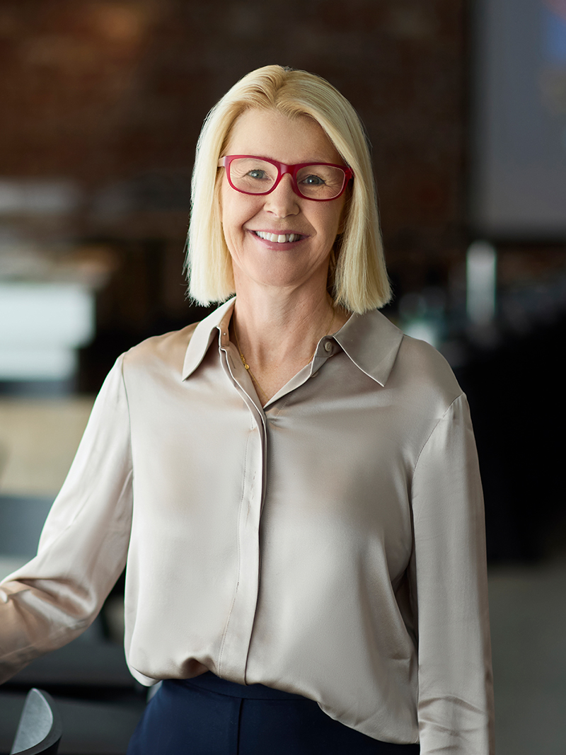 Professionally dressed individual wearing a light button-up blouse in a modern indoor setting.