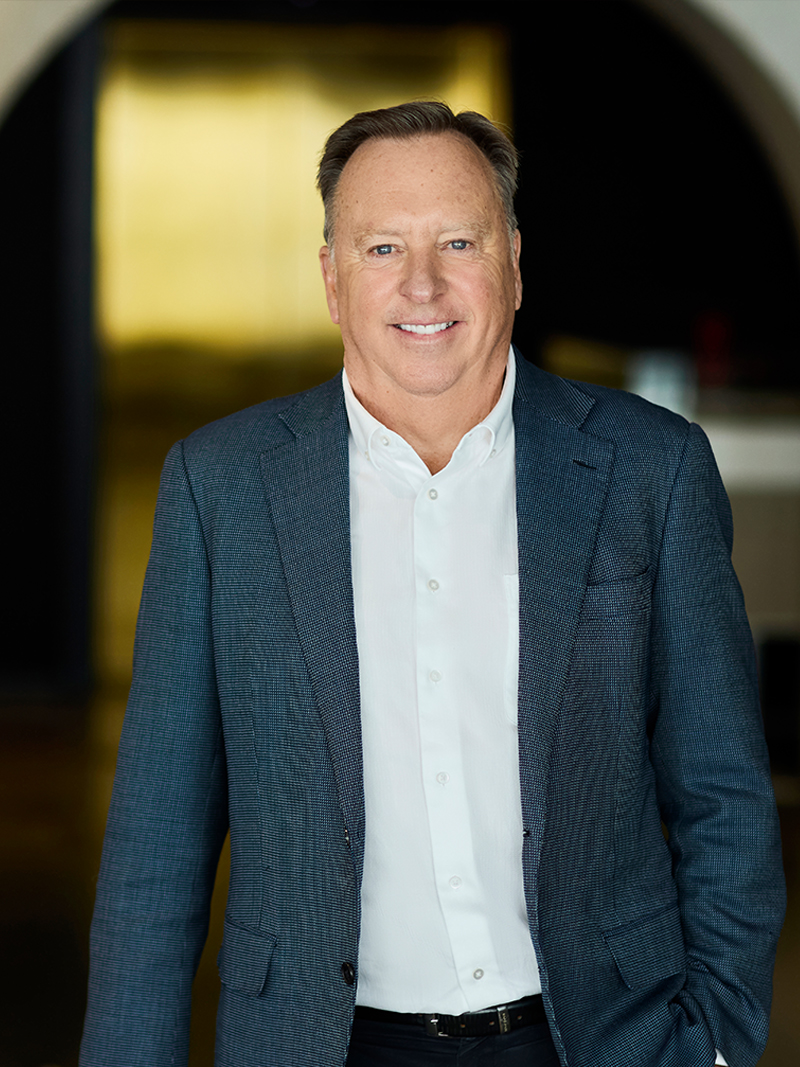 Professionally dressed individual in a blue blazer and white shirt standing in a modern indoor setting.