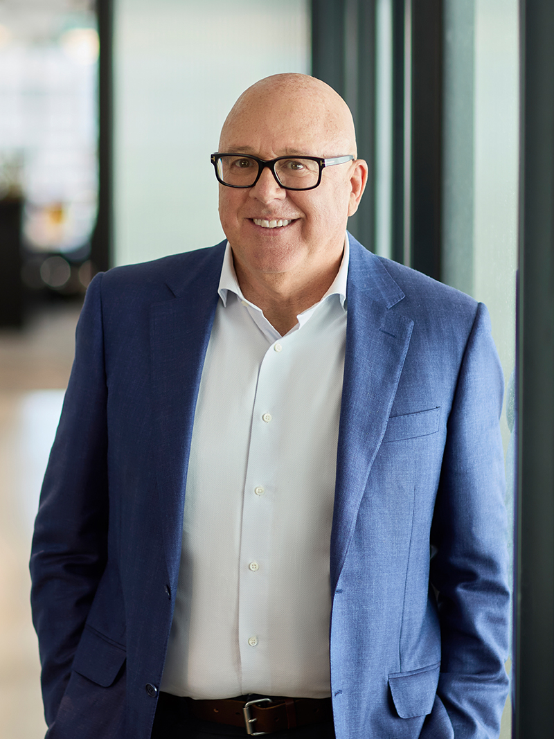 Professionally dressed individual in a blue blazer and white shirt standing in a modern office with natural light.