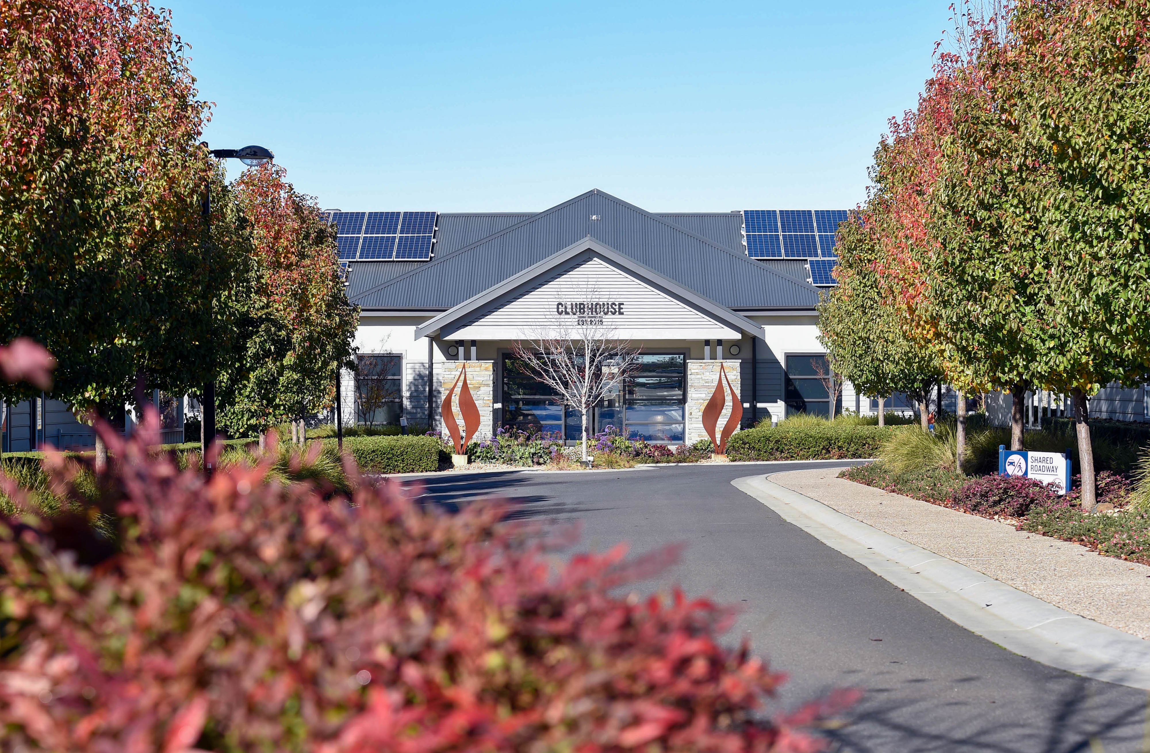 Centered clubhouse beyond landscaped drive with red foliage in foreground.
