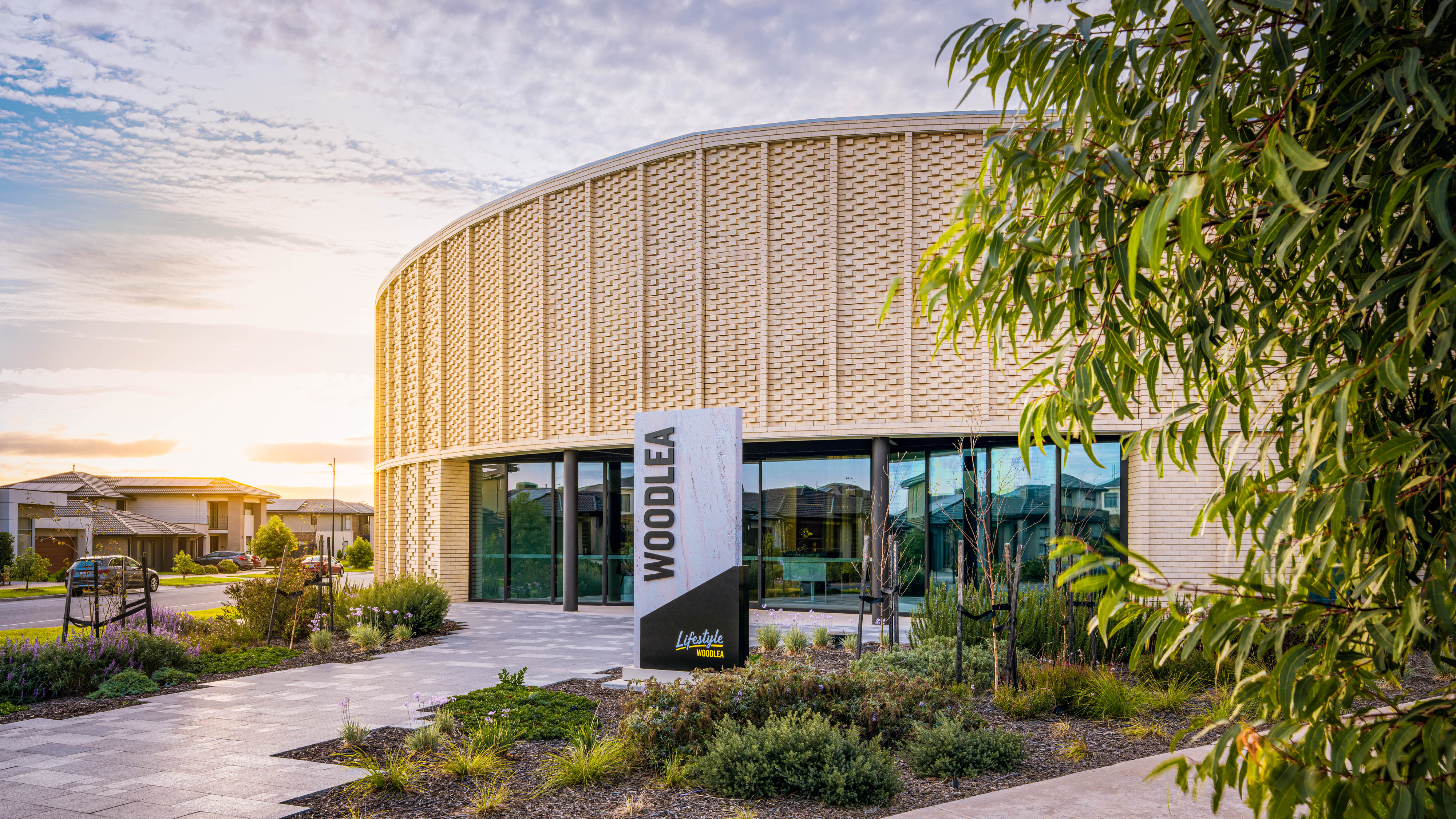 Lifestyle Woodlea clubhouse exterior at sunset with landscaped gardens and modern circular brick design.