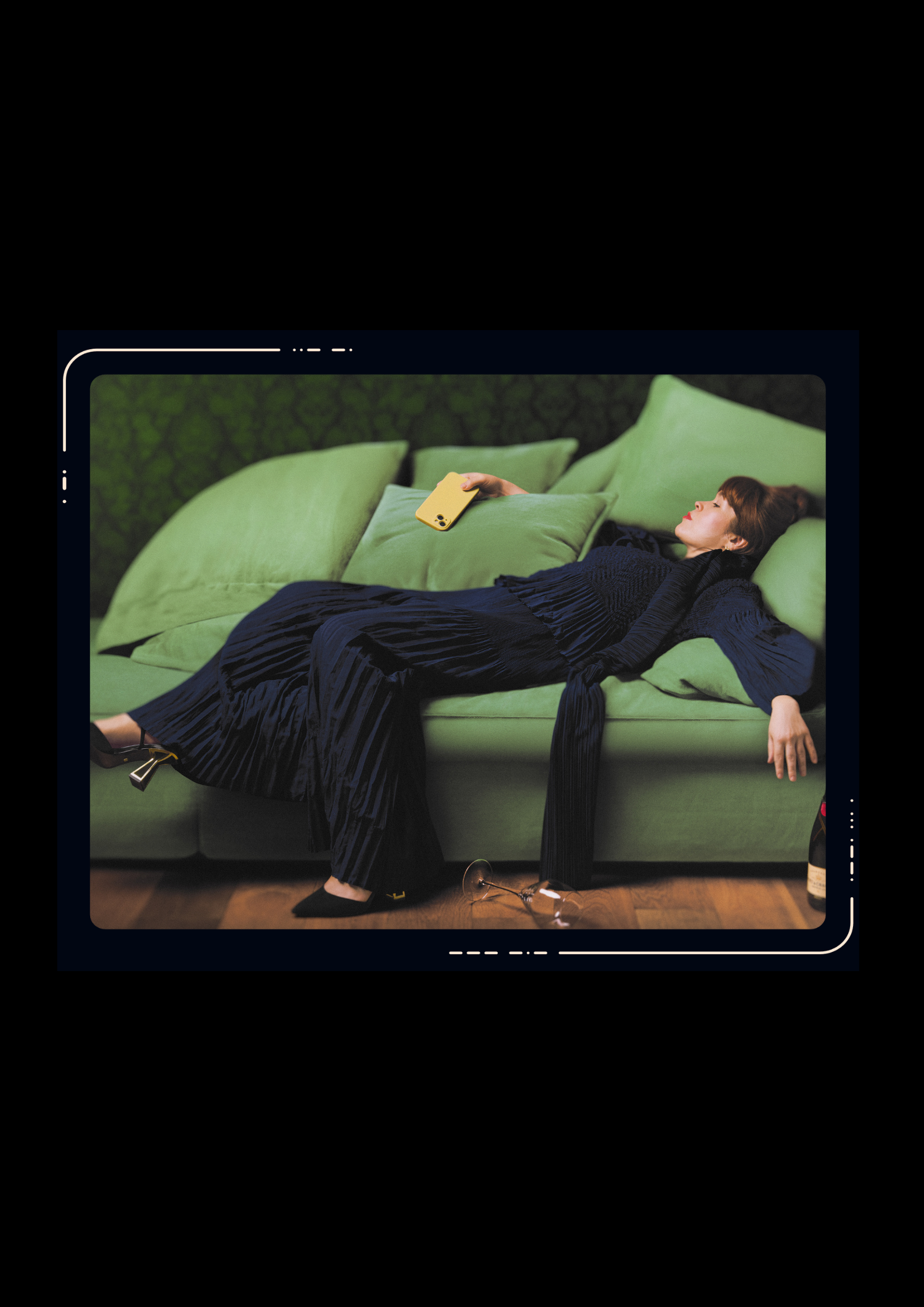 Woman in navy wide-leg trousers and matching top lying on a green sofa, holding a yellow phone, heels on, glasses on the floor.