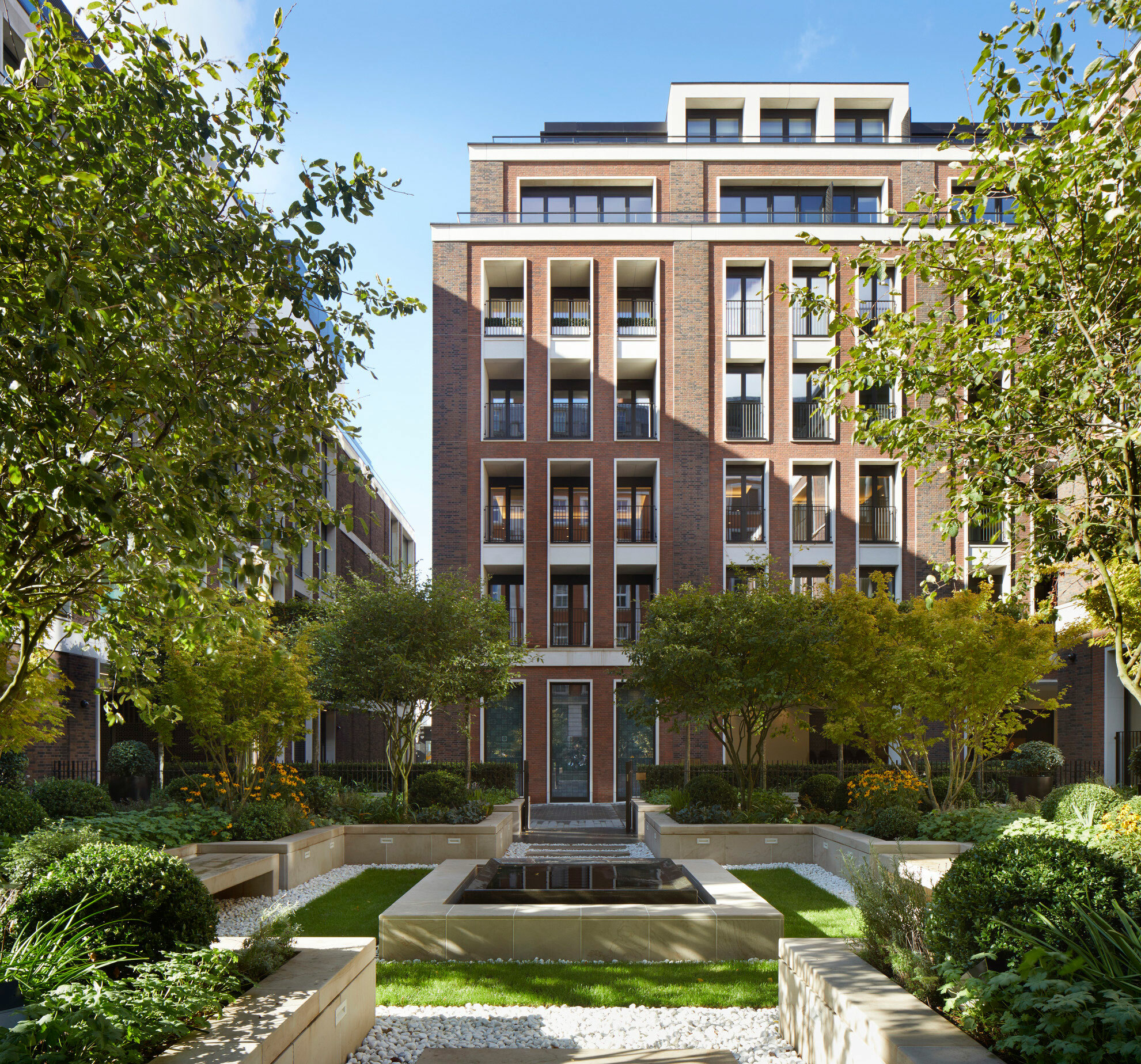 Luxury apartment building with courtyard and trees in foreground.