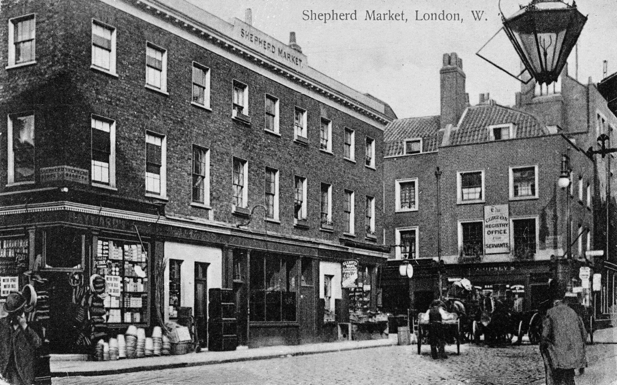 A black and white photograph of Shepherd Market in the 1900's with a few shops and people.