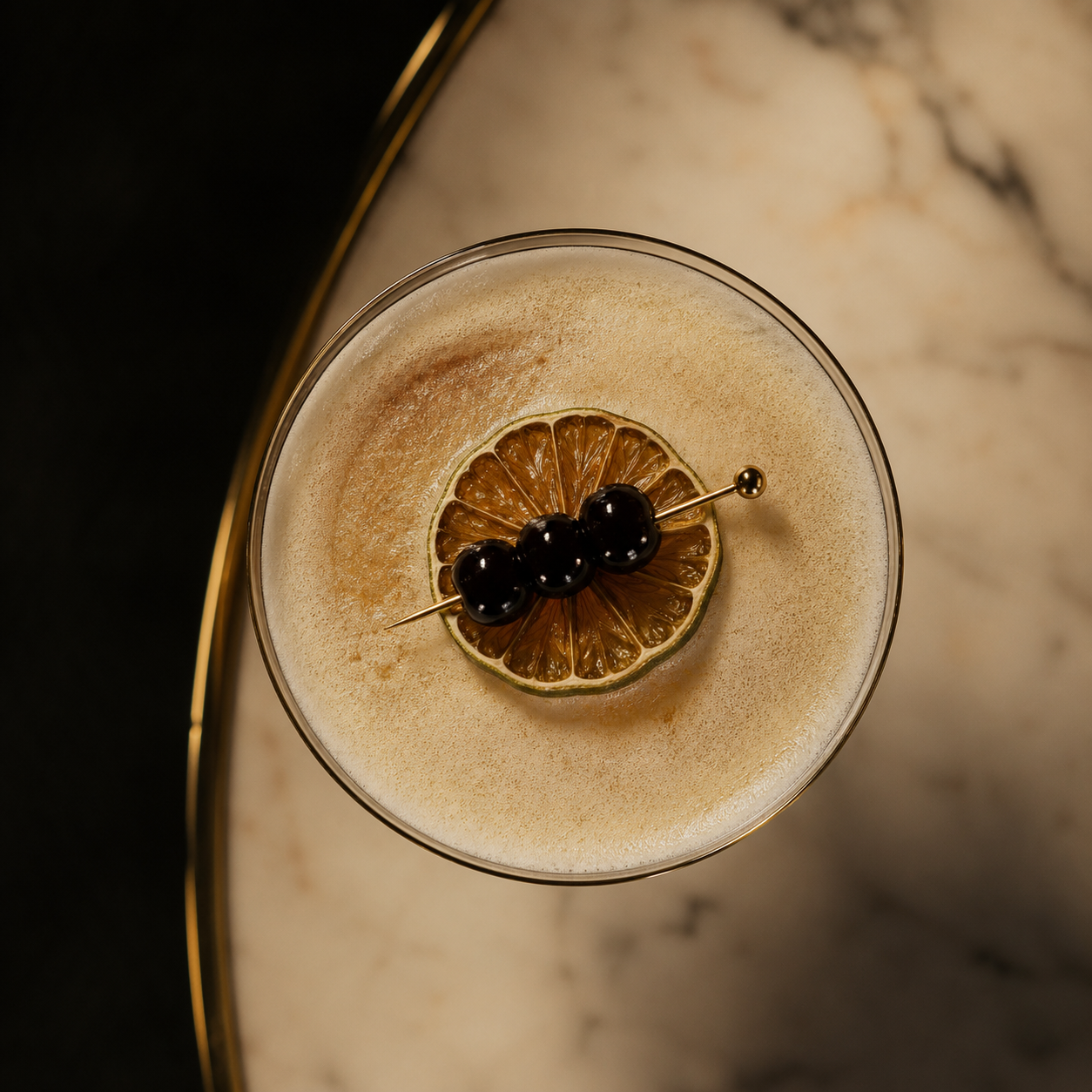 Overhead view of a foamy cocktail in a coupe glass, garnished with a dried citrus slice and three black berries on a cocktail pin.