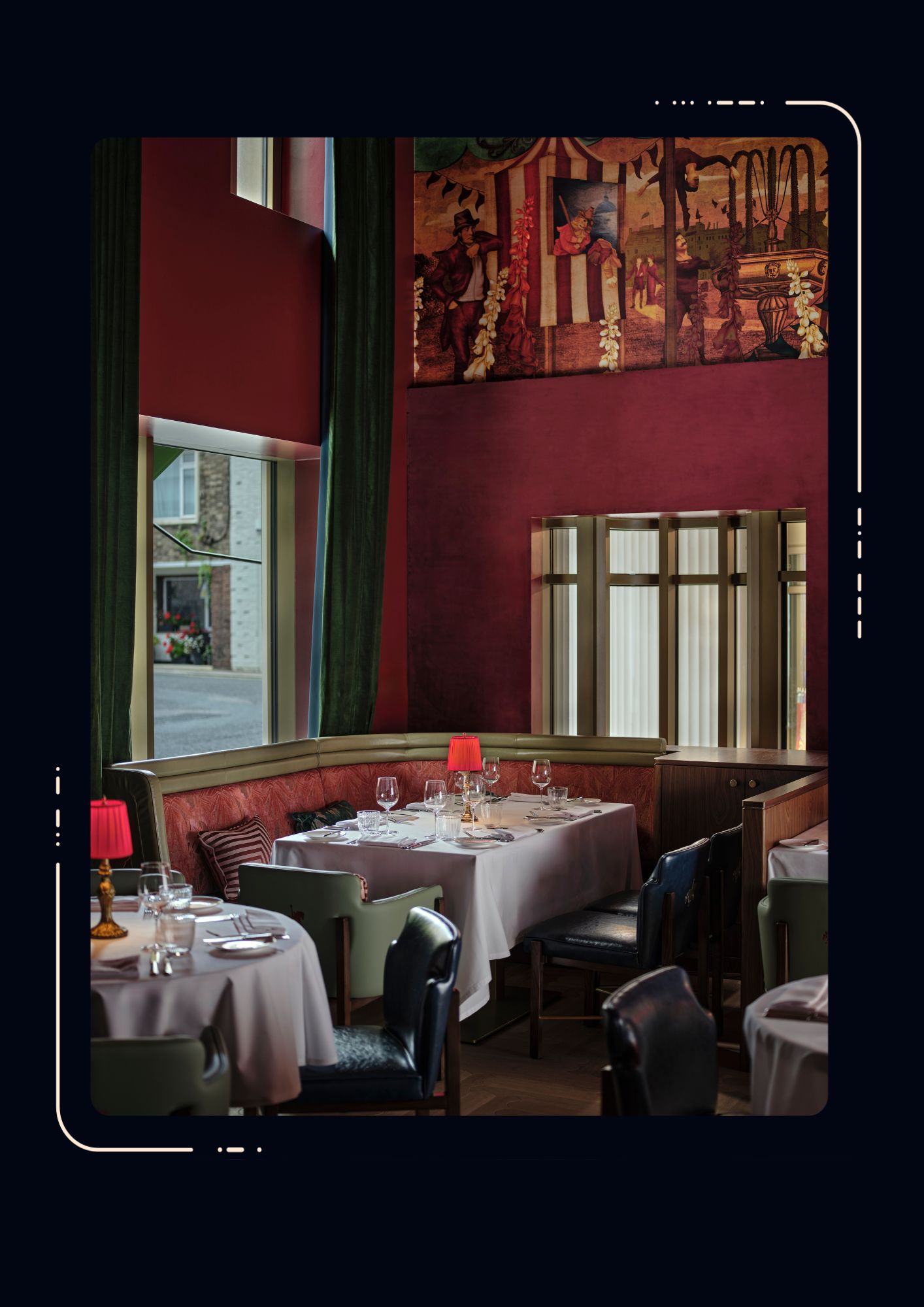 Restaurant interior with deep red walls, white-clothed tables, red lamp shades, leather chairs, curved banquette seating and a large mural above the windows.