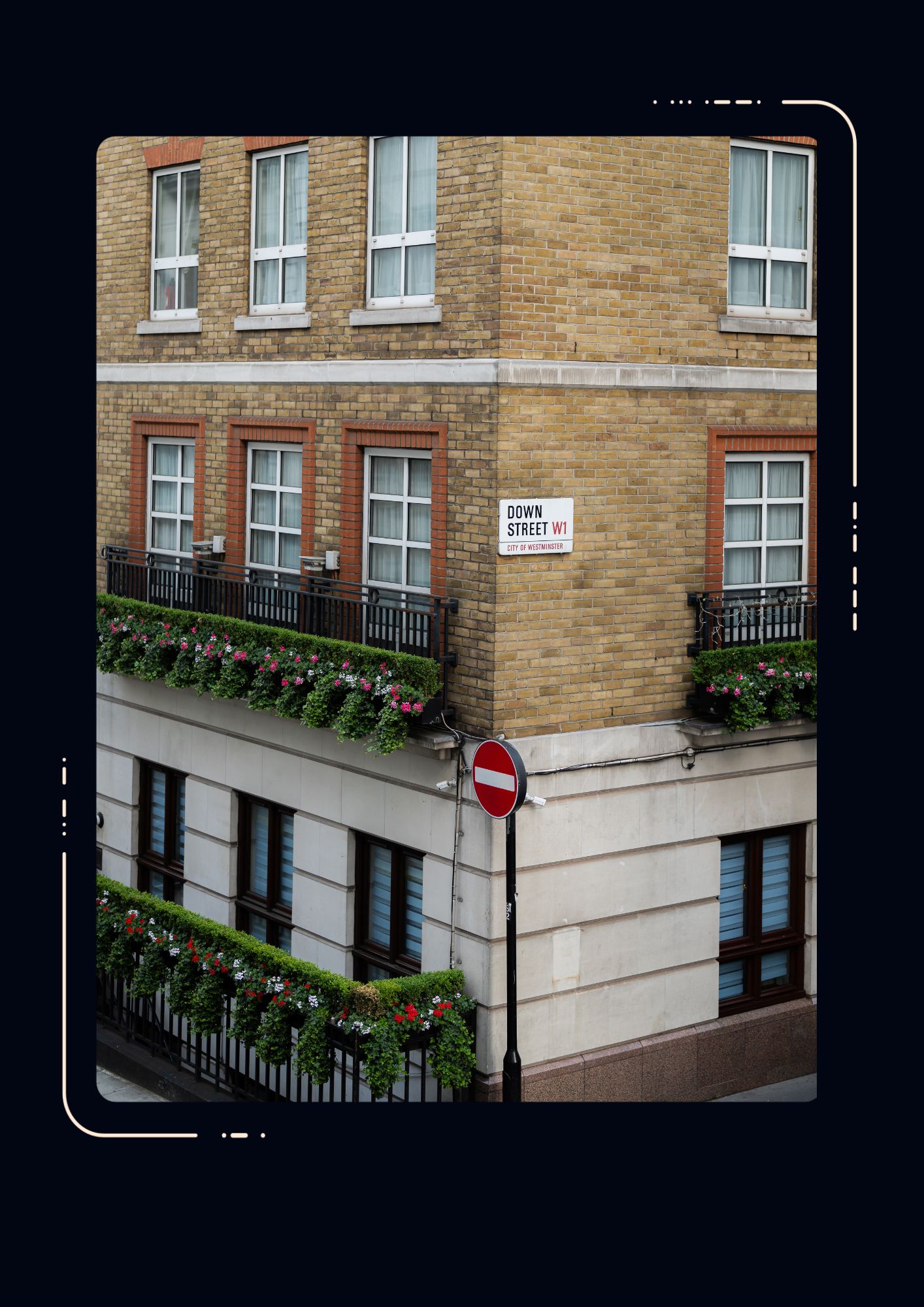 Corner of a London brick building on Down Street W1, with flower-lined balconies, sash windows, and a no-entry sign below.