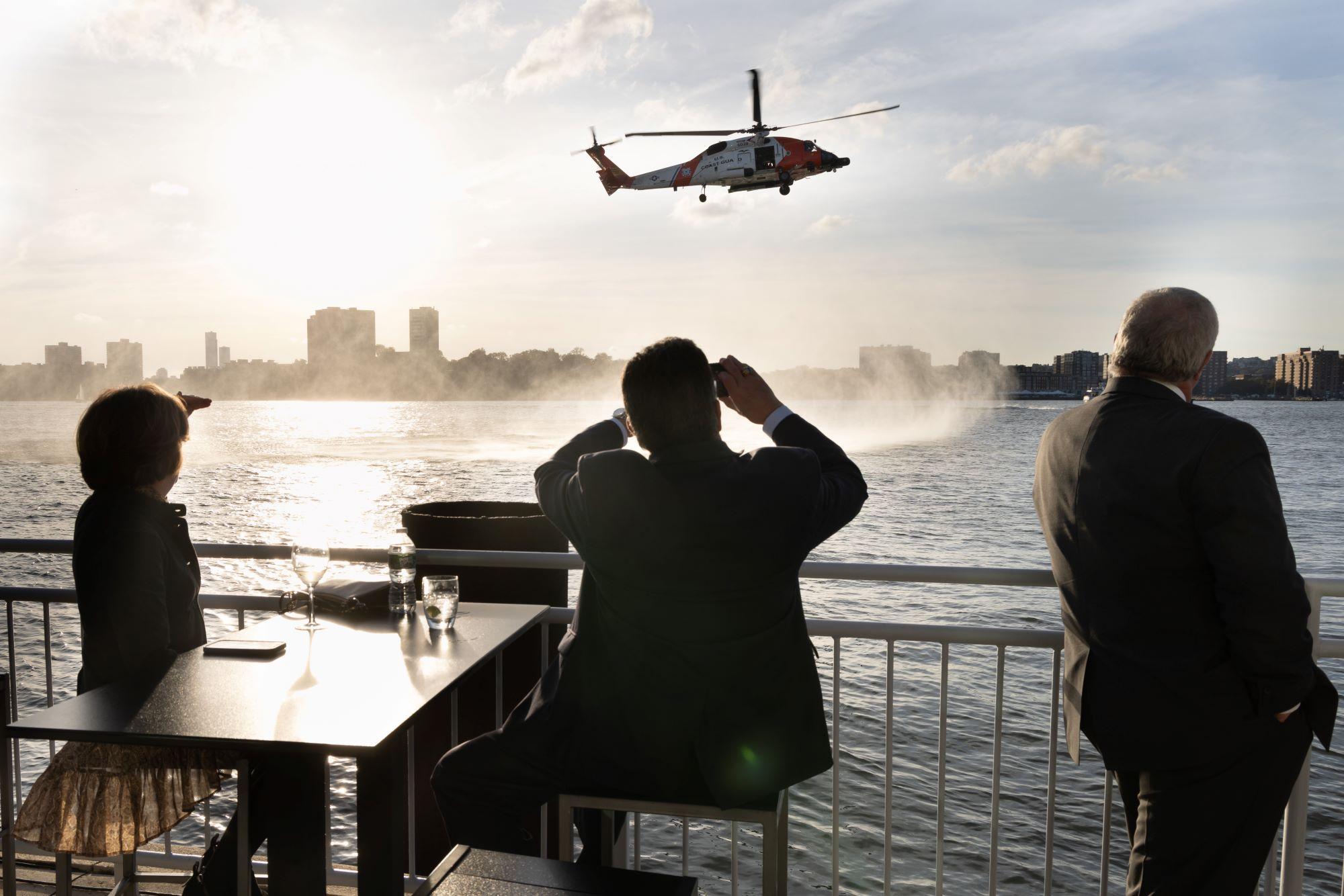 A person takes a photograph of a helicopter flying over the Hudson River in New York