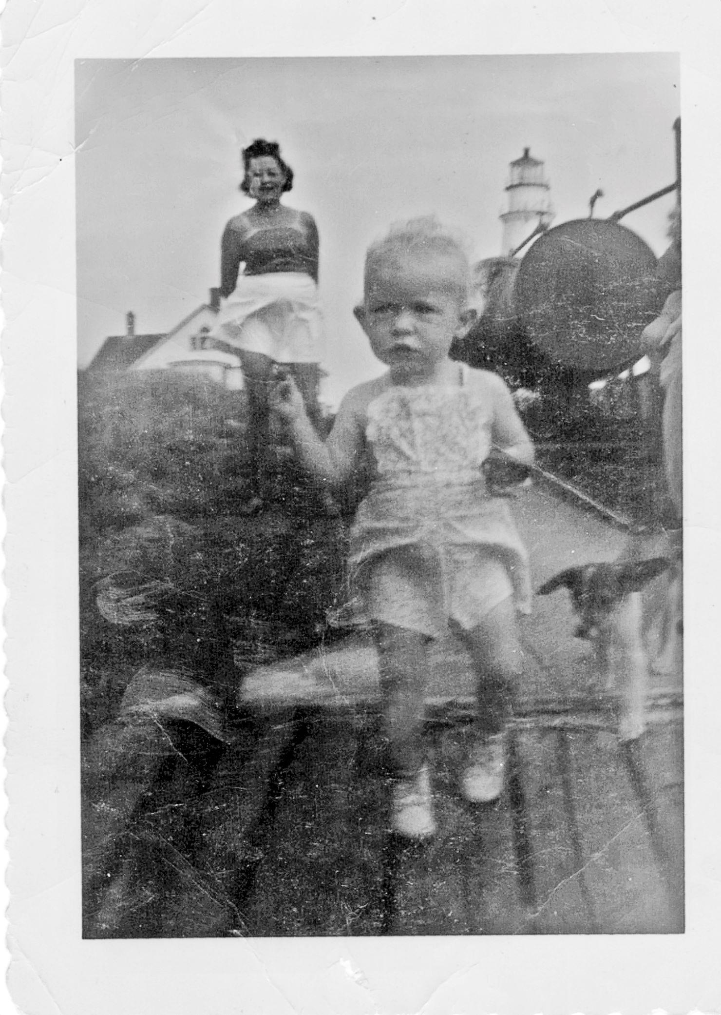 A child and her mother on Little Brewster Island with the lighthouse in the background.