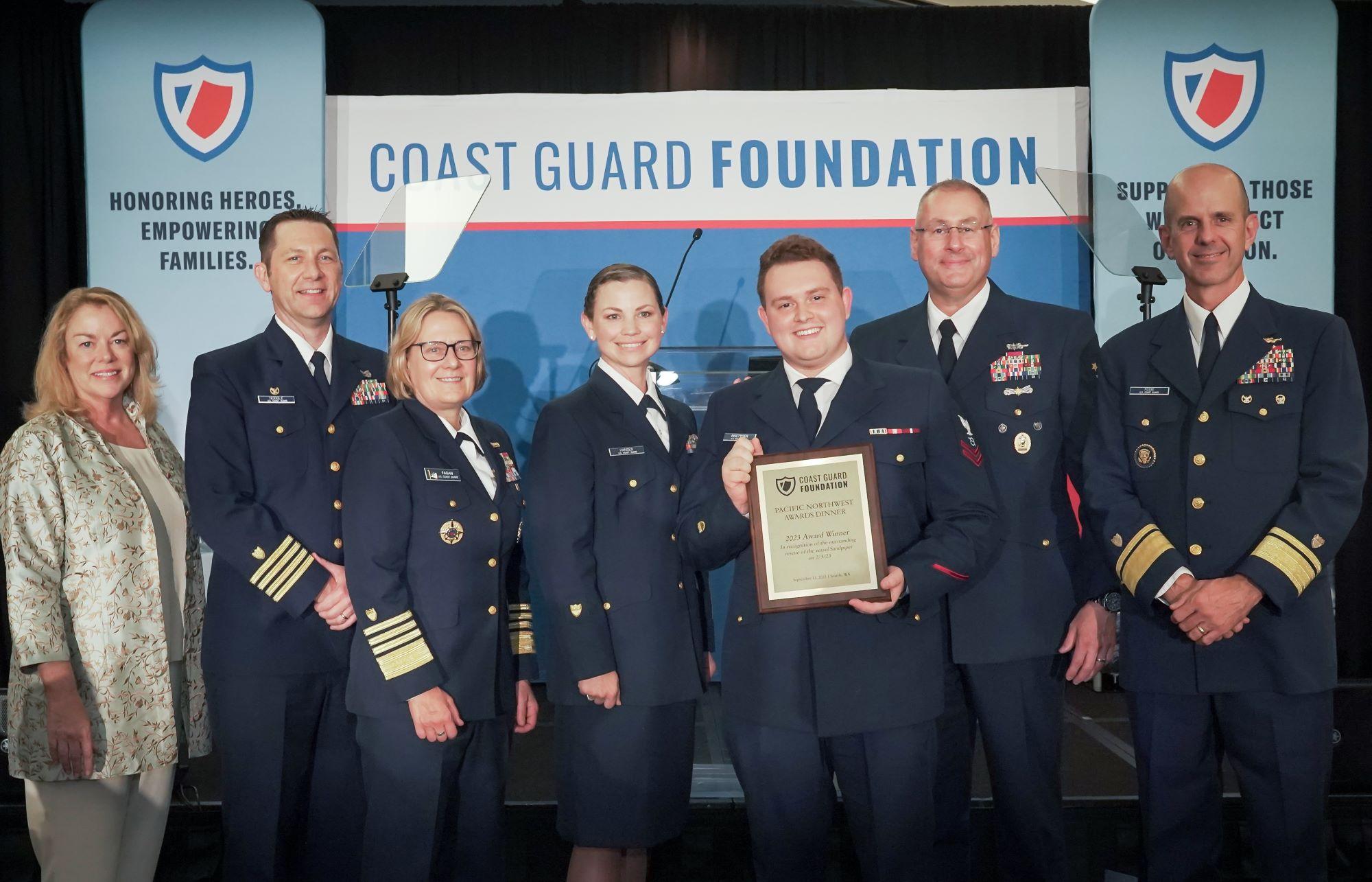 Coast Guard crew members being honored for a rescue pose in front of a stage with Coast Guard and Foundation leaders.