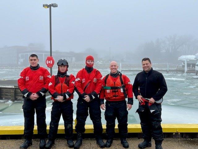 Five Coast Guard members pose in protective gear on a pier