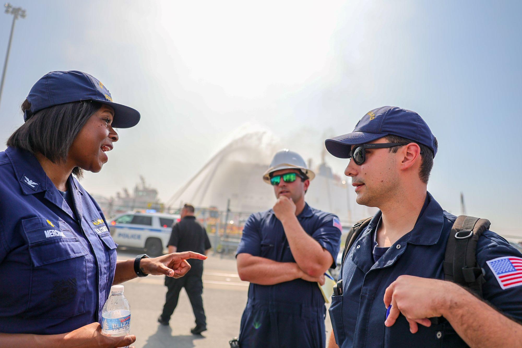 Photo of Coast Guard members and response personnel with fire fighting water in the background.