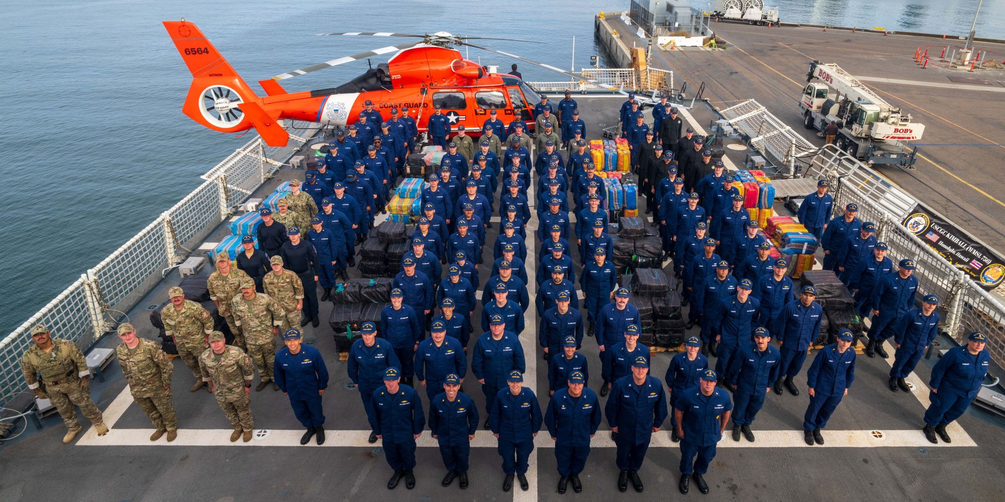 Crew members from the U.S. Coast Guard Cutter Kimball (WMSL 756), Tactical Law Enforcement Team South, U.S. Coast Guard Maritime Safety and Security Team Los Angeles/Long Beach, and Helicopter Interdiction Tactical Squadron Jacksonville all stand at attention during a drug offload in San Diego April 24, 2025.