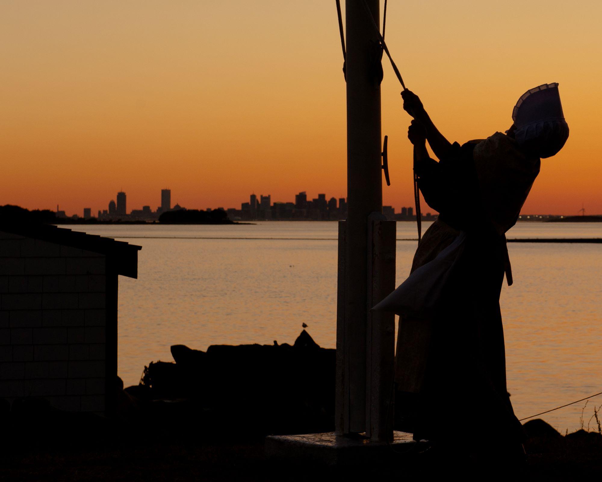 Lighthouse keeper at a flag pole with the Boston skyline in the background.