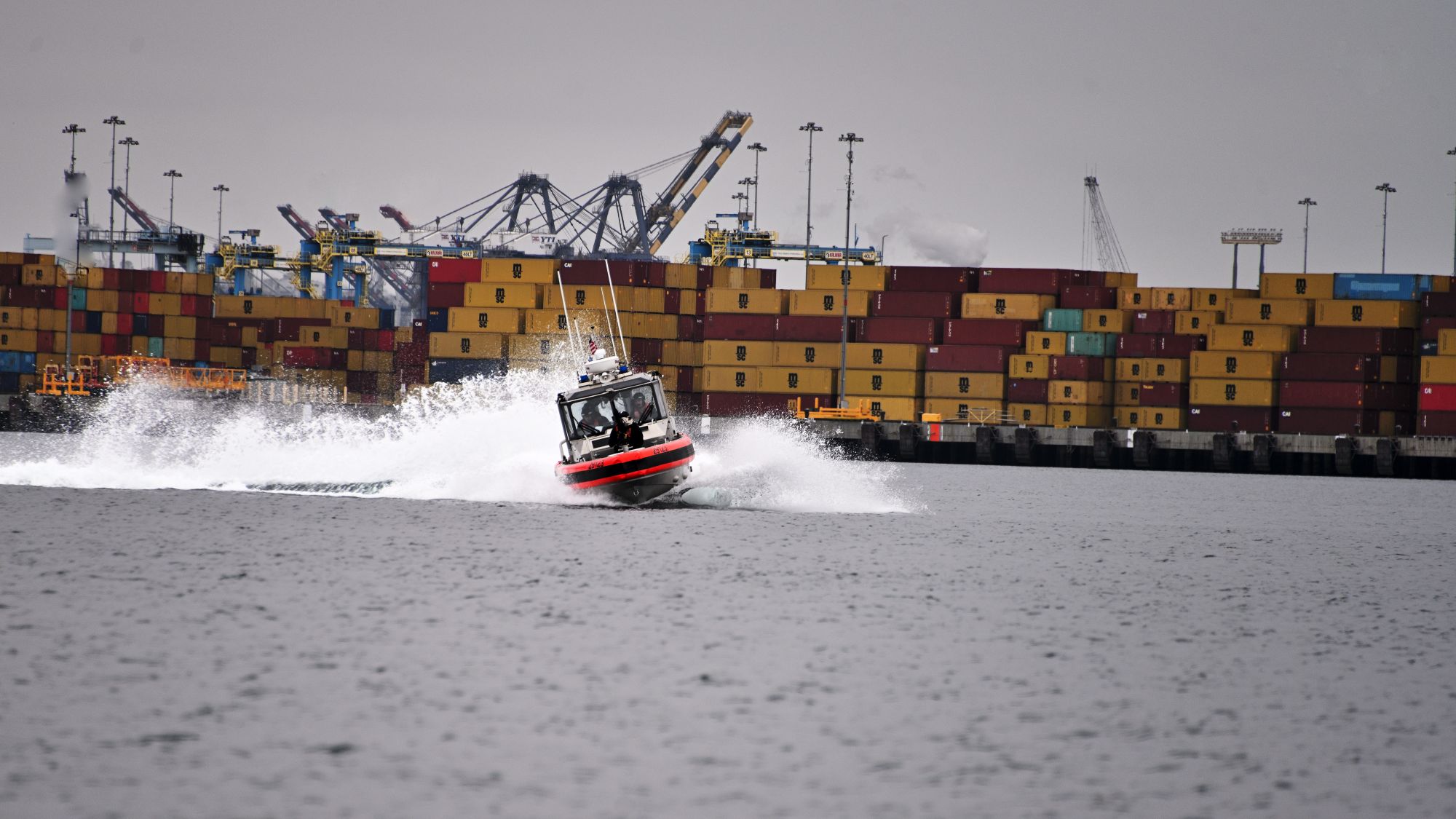 A boat maneuvers in front of a container ship.