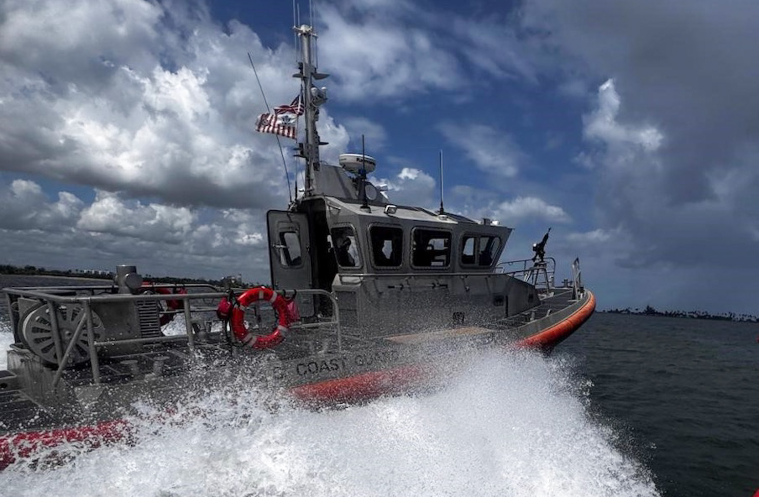 U.S. Coast Guard boat rushes through water, kicking up white seafoam.