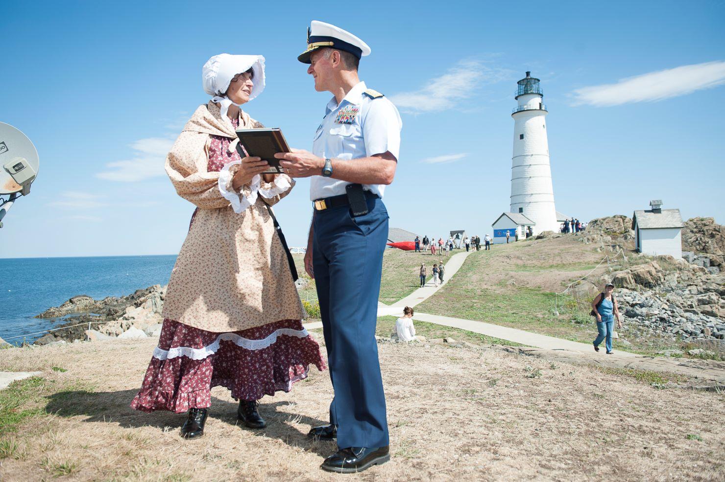 A lighthouse keeper and Coast Guard officer standing with a lighthouse in the background.