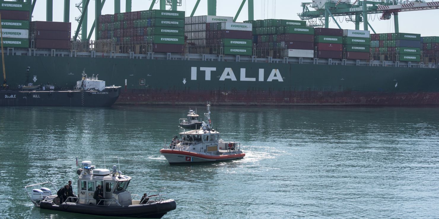 Two boats in front of a container ship.