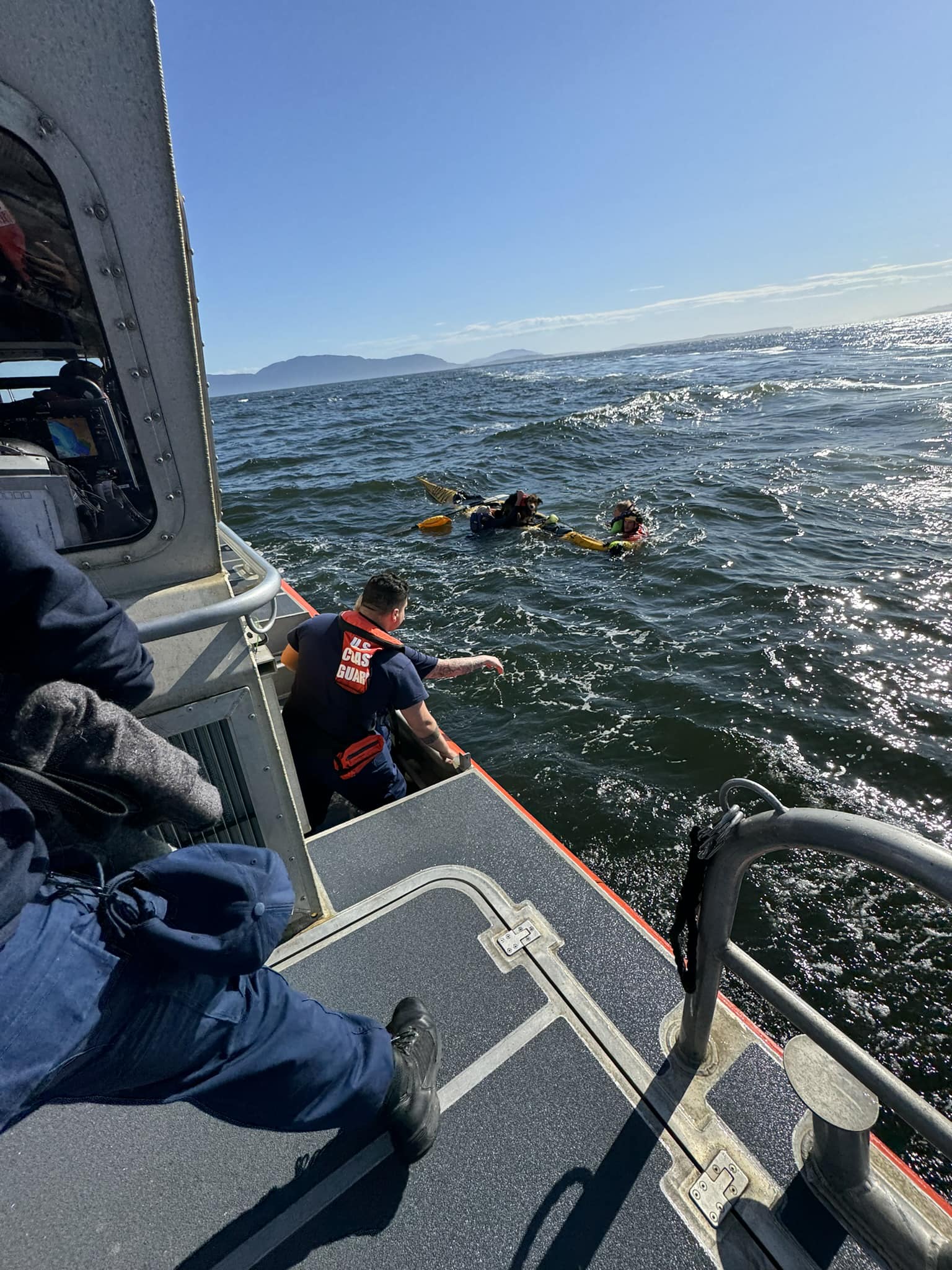 Coast Guard member on a boat rescue people from their swamped kayaks.