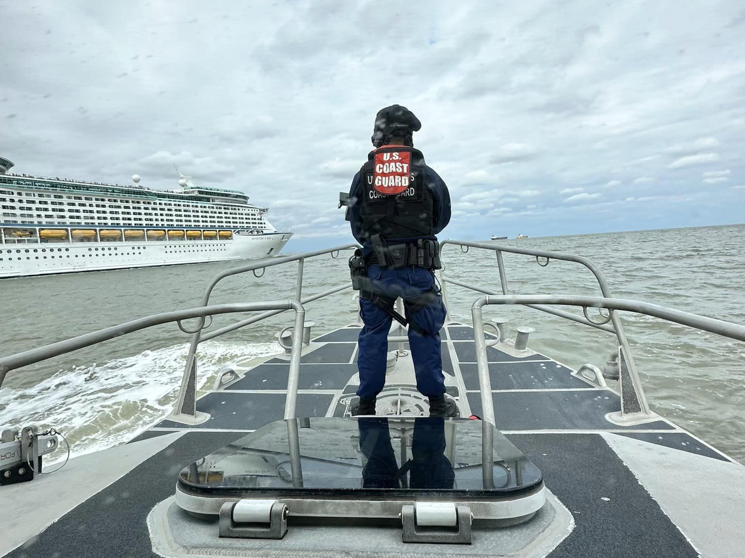 A Coast Guard member on the bow of a boat with a cruise ship in the background
